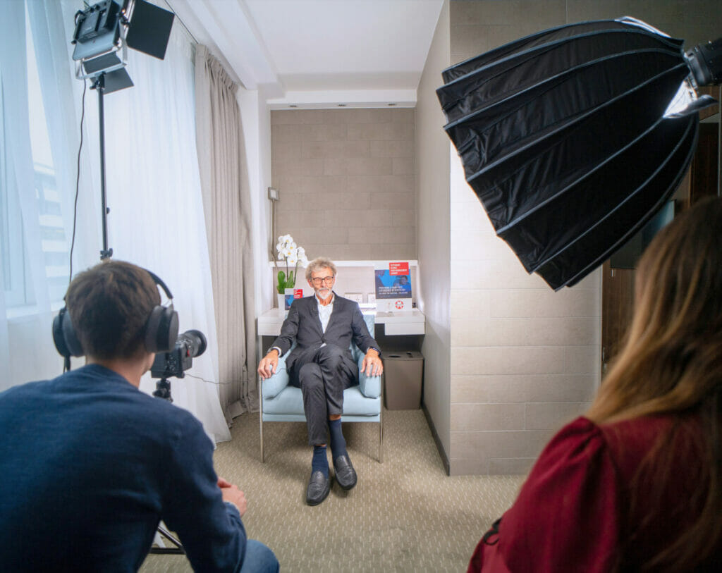 Un homme assis est interviewé par équipe de tournage